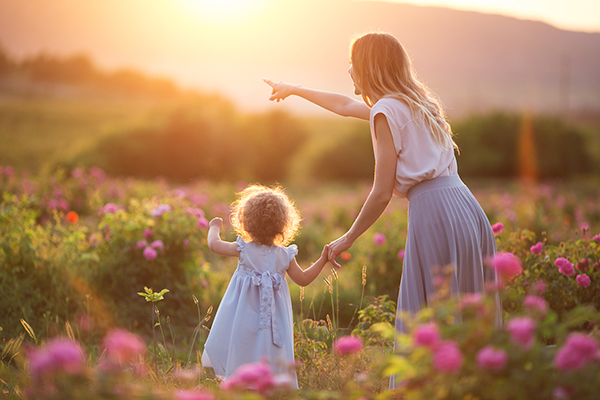 Beautiful child girl with young mother are wearing casual clothes walking in roses garden over sunset lights