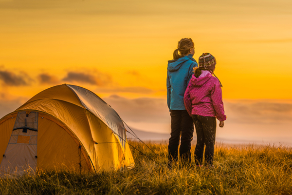 Children camping on mountain ridge looking into golden sunset panorama