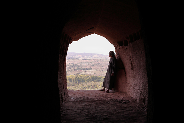 hermit man with robe in the entrance of a old cave in front of a valley