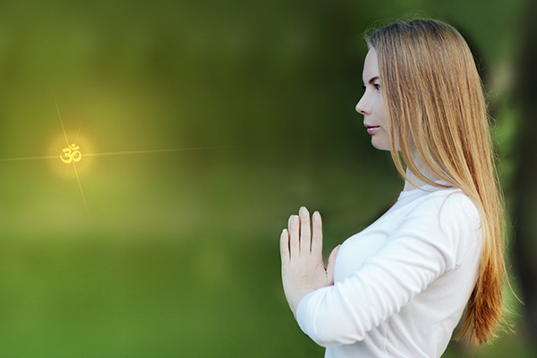 Woman in white clothes doing yoga, hands at the heart chakra in front of the chest namaste at sunset, on a blurred lush green background. side view