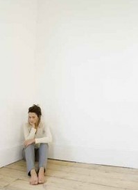 A young woman sitting in the corner of an empty room